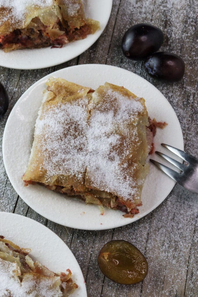 Delicious plum strudel slice on a plate, dusted with sugar.